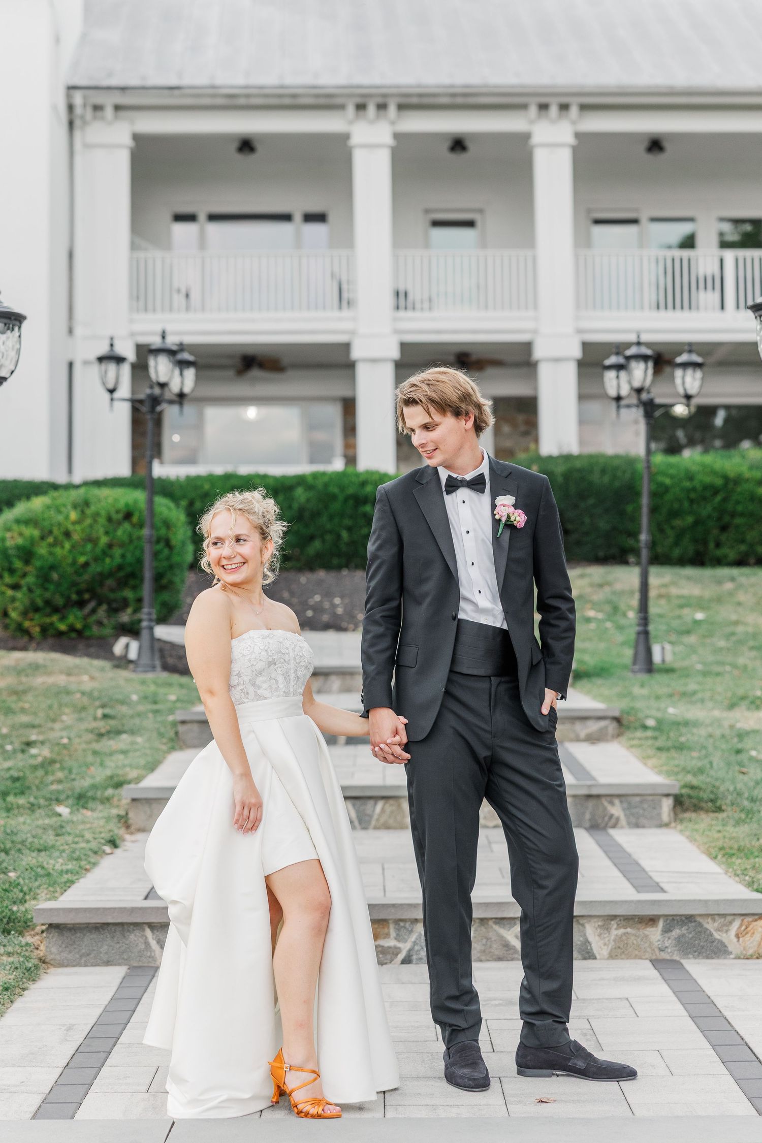 Wedding couple posing on stone steps in front of a white columned mansion.