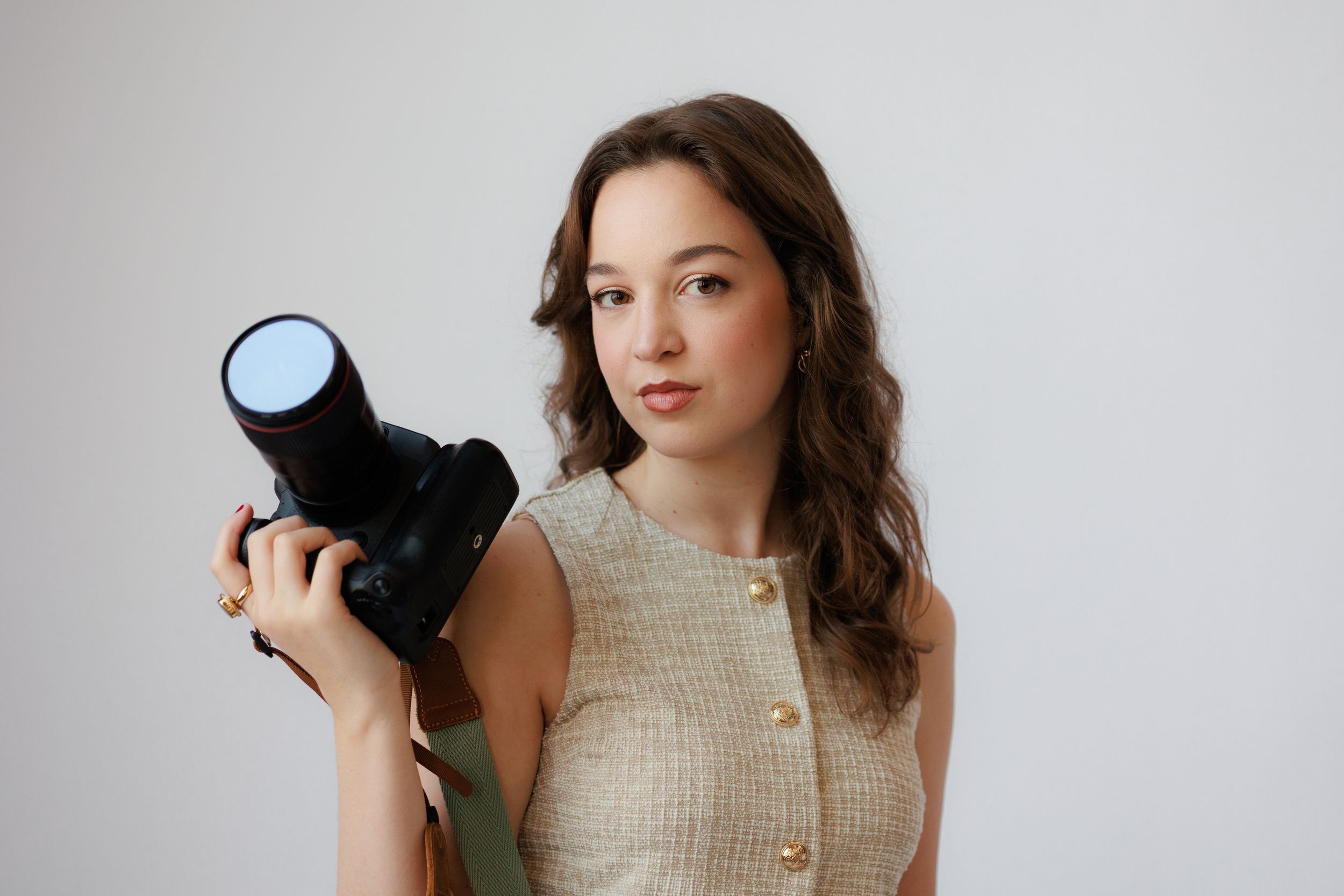 Professional photographer holding black DSLR camera against neutral background in studio setting.