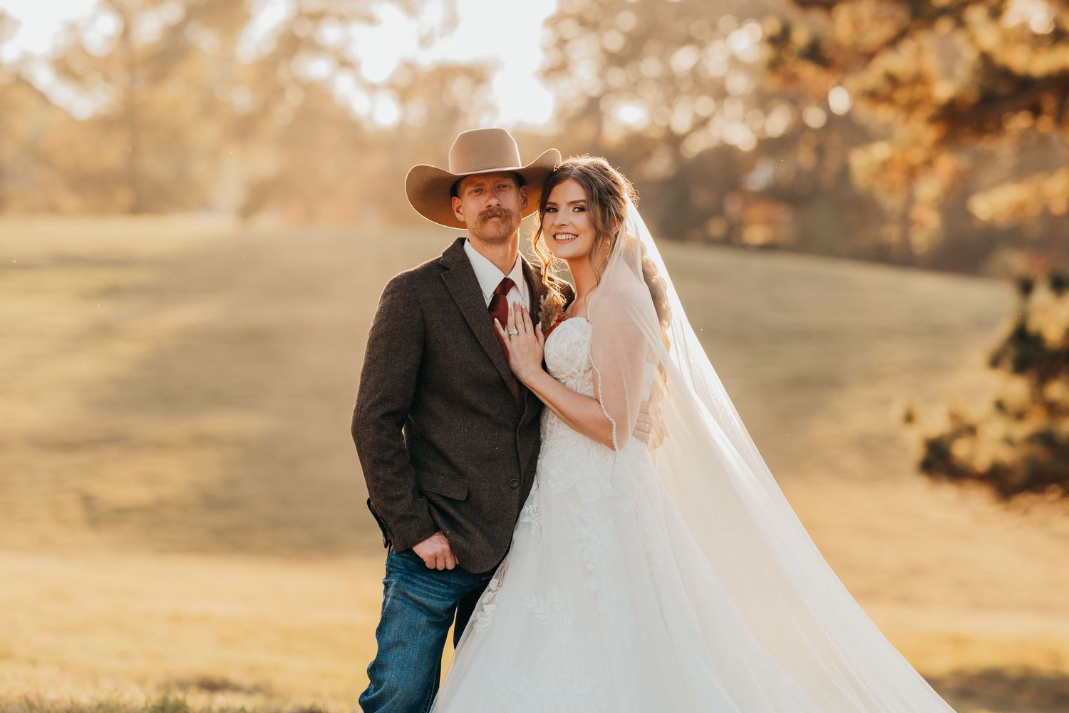 Couple in wedding attire embraces during golden hour in a romantic outdoor autumn setting.