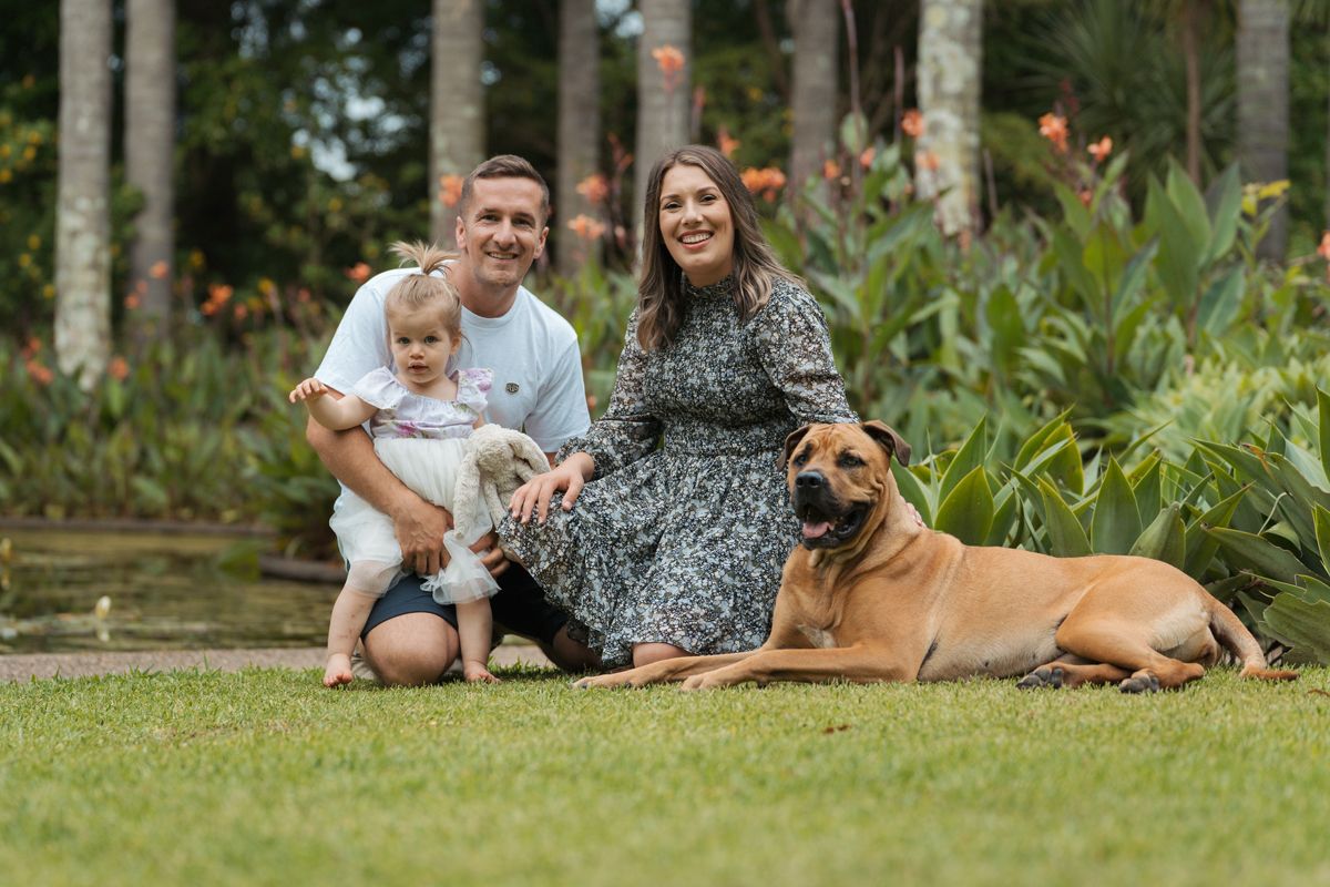 A family and their  Mastiff cross rescue dog relaxing together on green grass in Fagan Park during a family photoshoot in Sydney