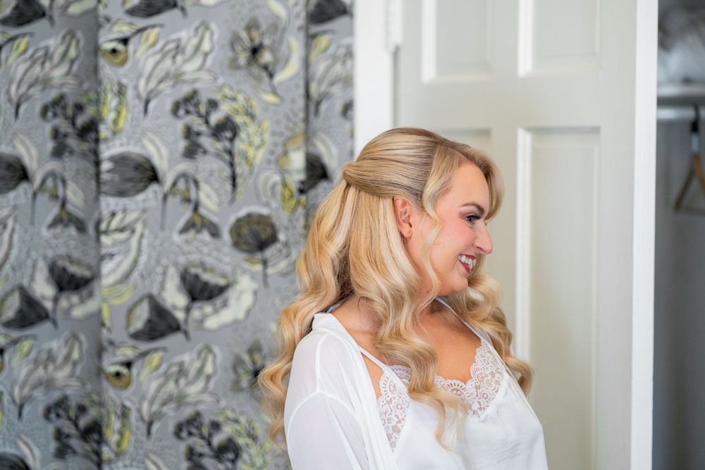 Woman in white sweater poses against floral wallpaper background in bright interior setting.