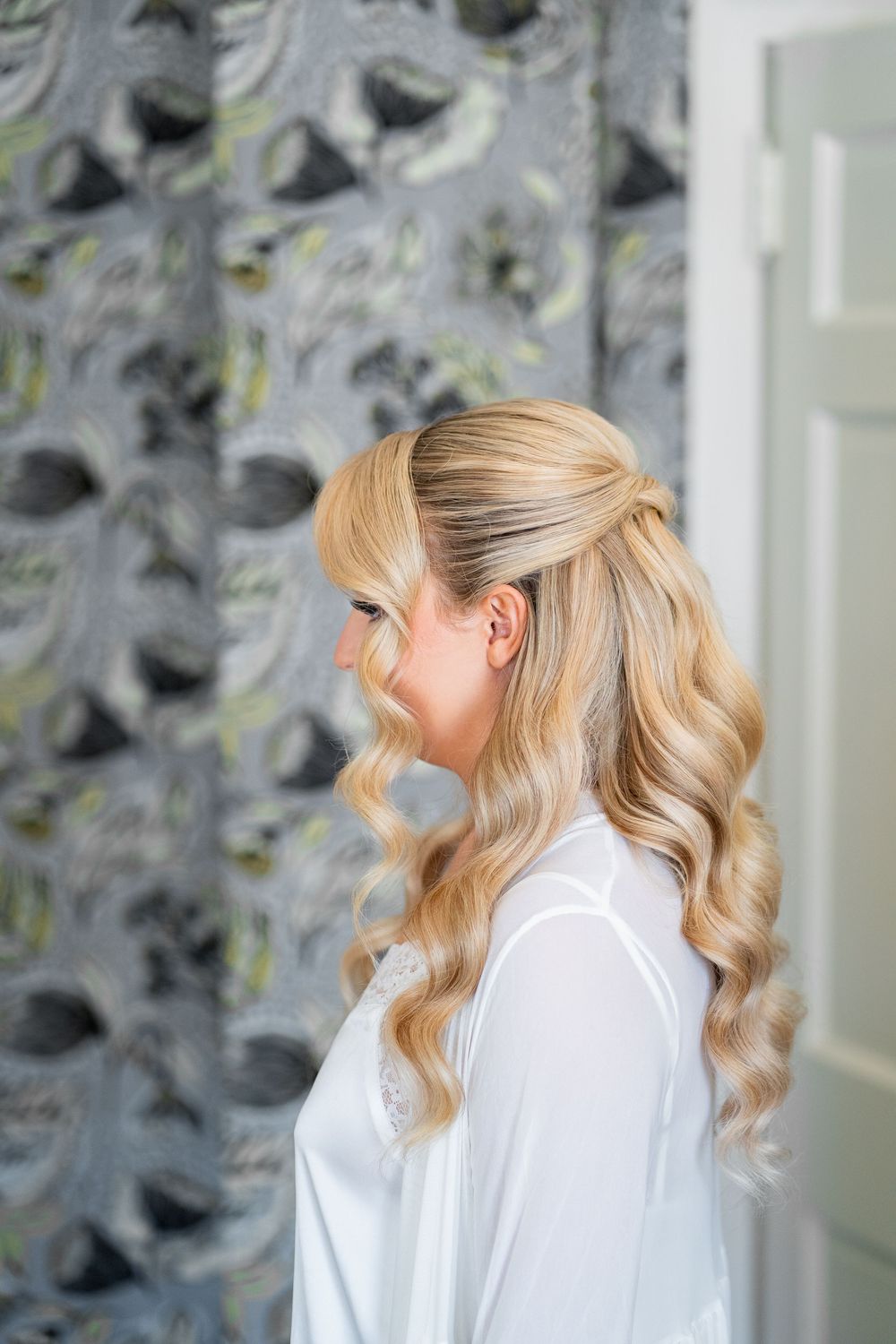 Side view of blonde hair styled in soft waves against a gray patterned wall background.