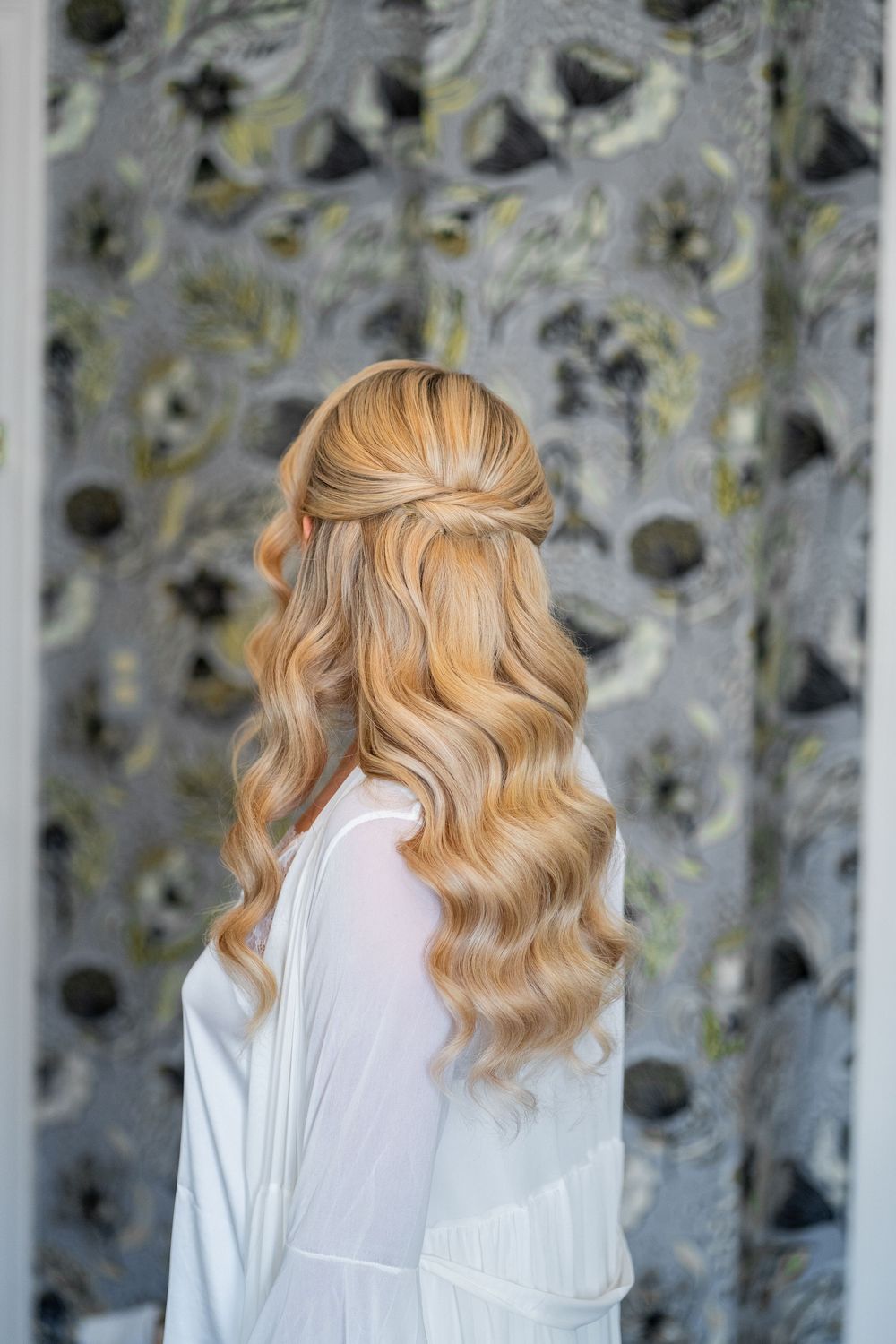Back view of blonde wavy hair styled in soft curls against a textured gray background.
