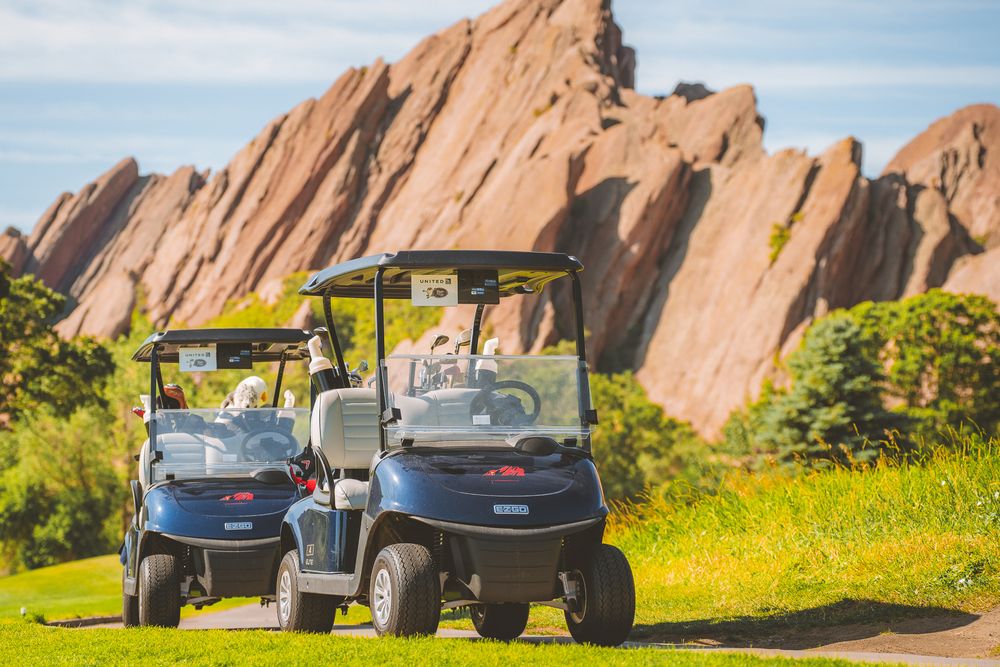 Scenic landscape of red rock formations with utility vehicles parked along a grassy path.