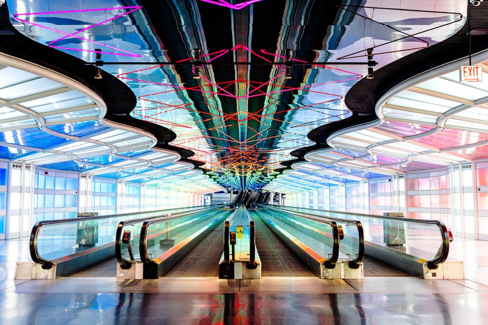 Colorful illuminated moving walkway tunnel with geometric patterns in an airport terminal.
