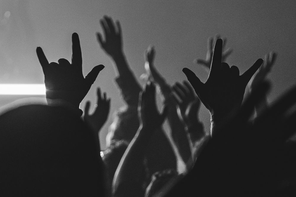 Silhouetted crowd with raised hands against dark background at a concert or event.