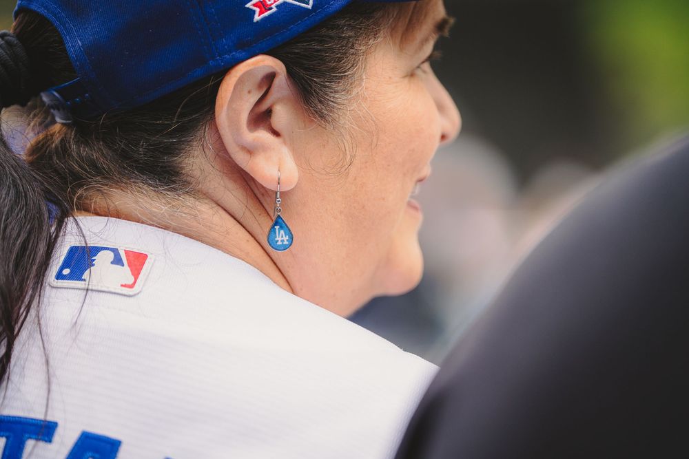 Woman wearing MLB blue cap and jersey with teardrop earring, smiling at outdoor baseball event.