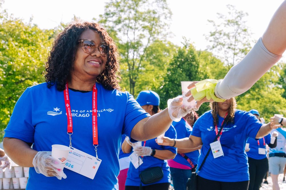 Volunteers in blue Bank of America Chicago shirts hand out cups at an outdoor charity walk event.