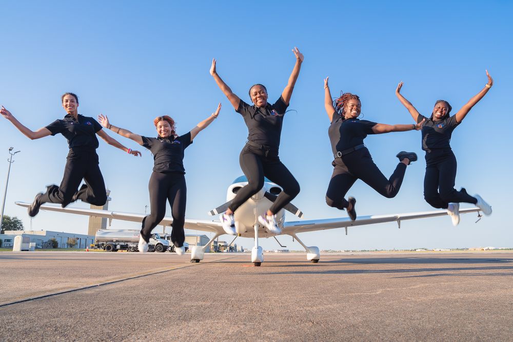 Group of people jumping in synchronized motion against blue sky background.