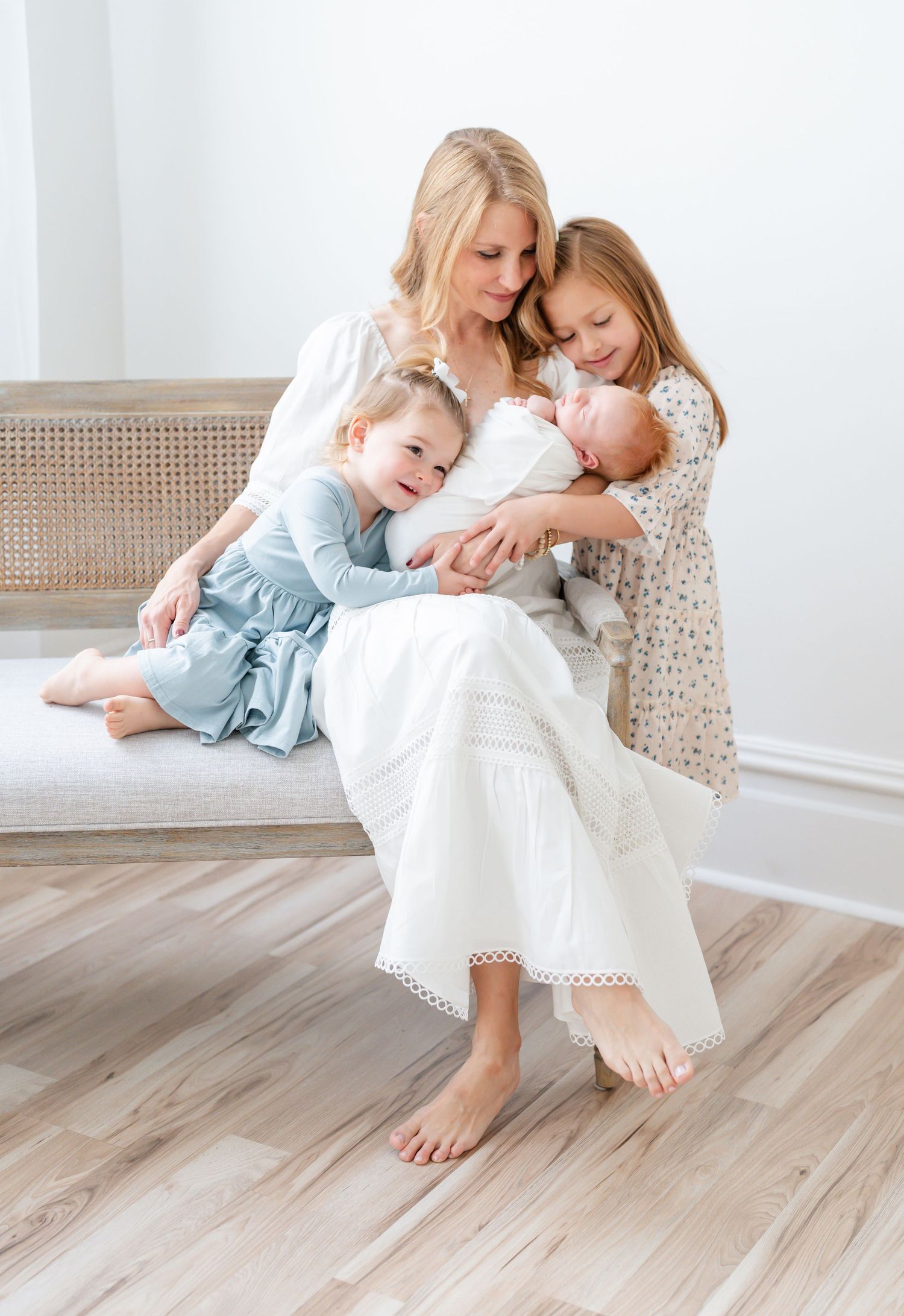 A tender moment shared between parent and child in white dresses sitting together on a light wooden floor.