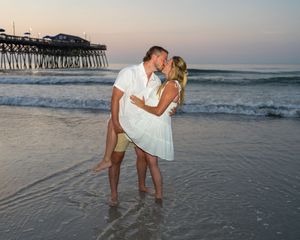 A romantic beach scene at sunset with a wooden pier in the background as waves roll onto the shore.