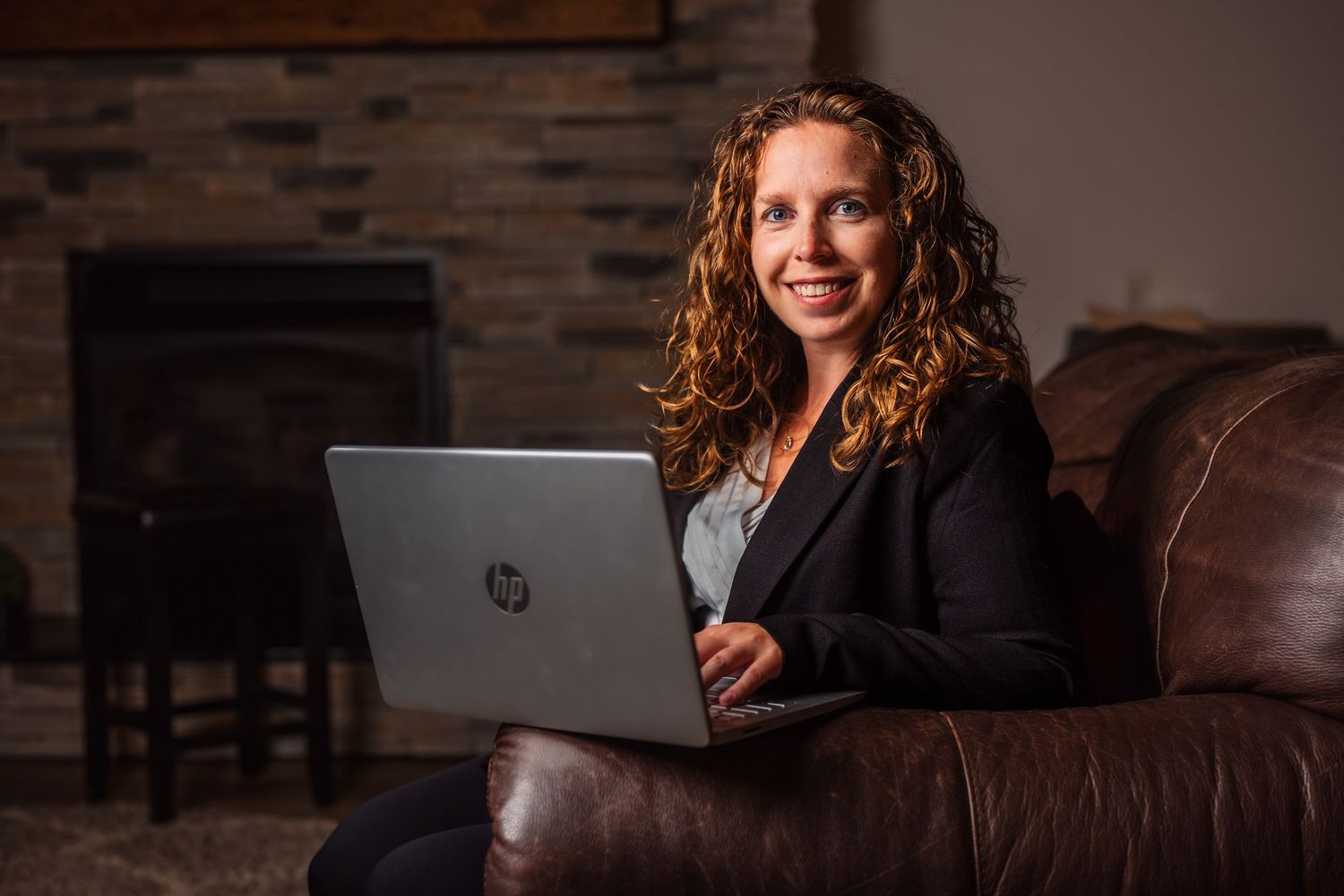 Person in business attire working on laptop while seated on brown leather couch.