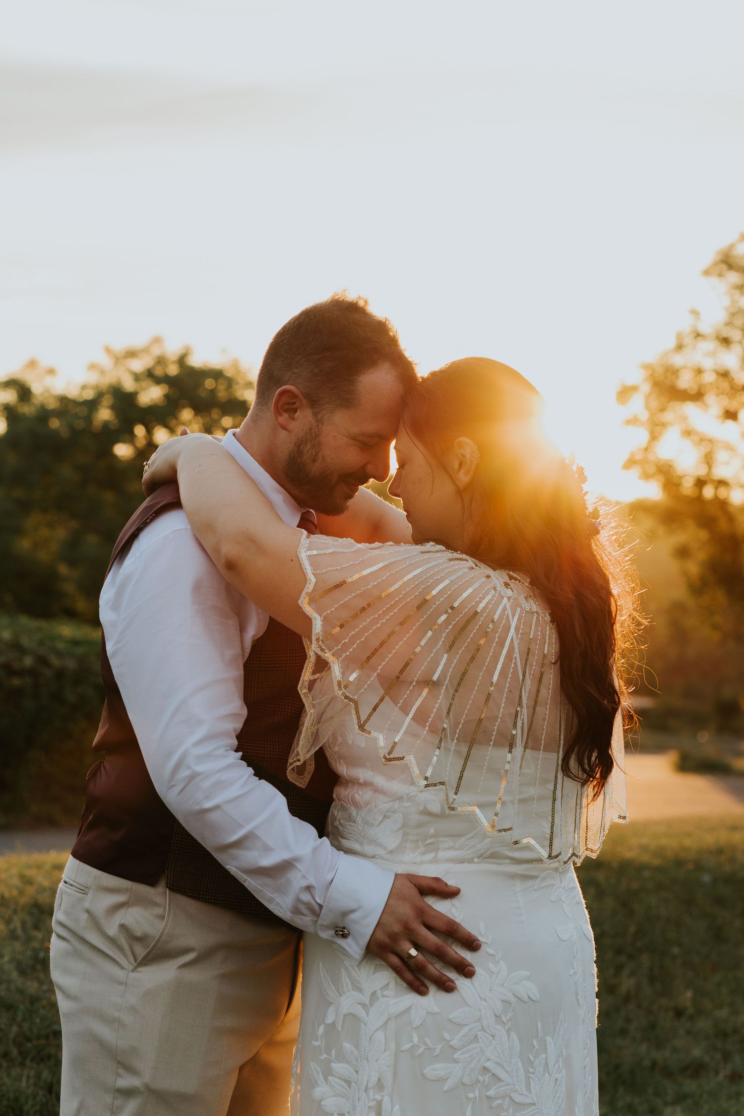 A couple dances on a grassy lawn in front of a historic white lighthouse tower with a modern glass extension.