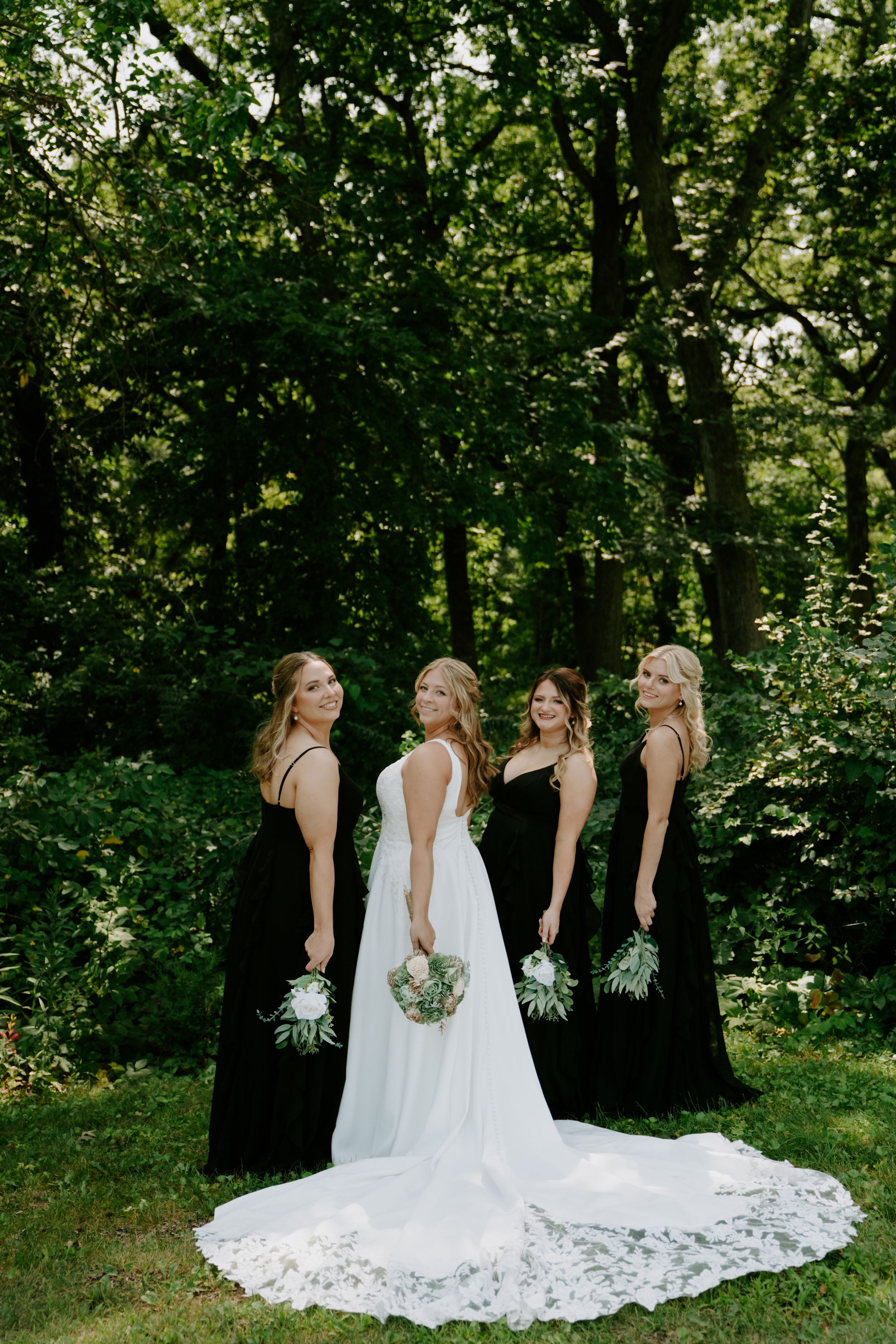 Wedding party in black and white dresses standing together in a wooded outdoor setting.