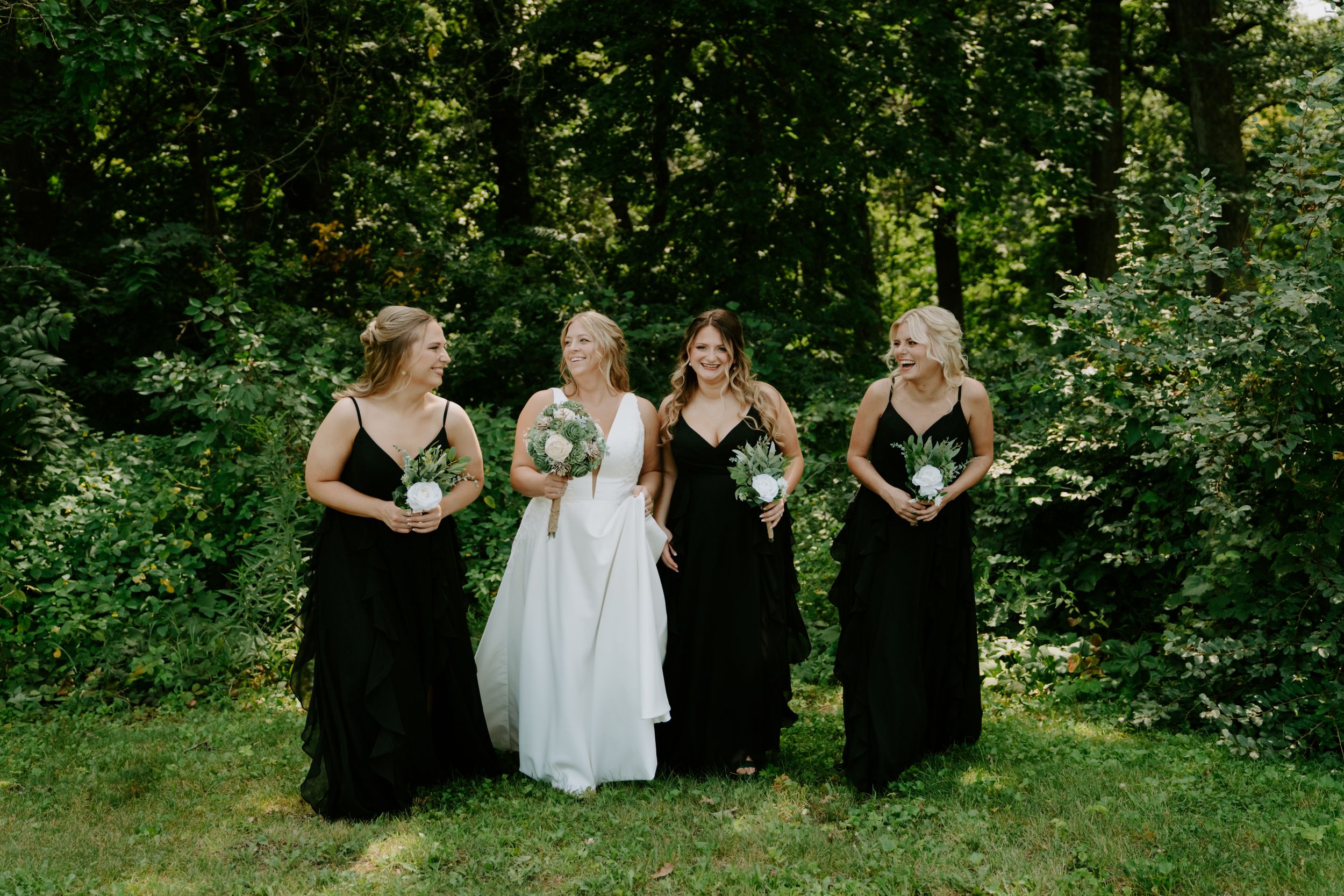 Bridal party in coordinated black and white attire posing in natural outdoor setting.