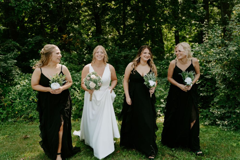 Wedding party in contrasting black and white dresses standing in a green forest setting.