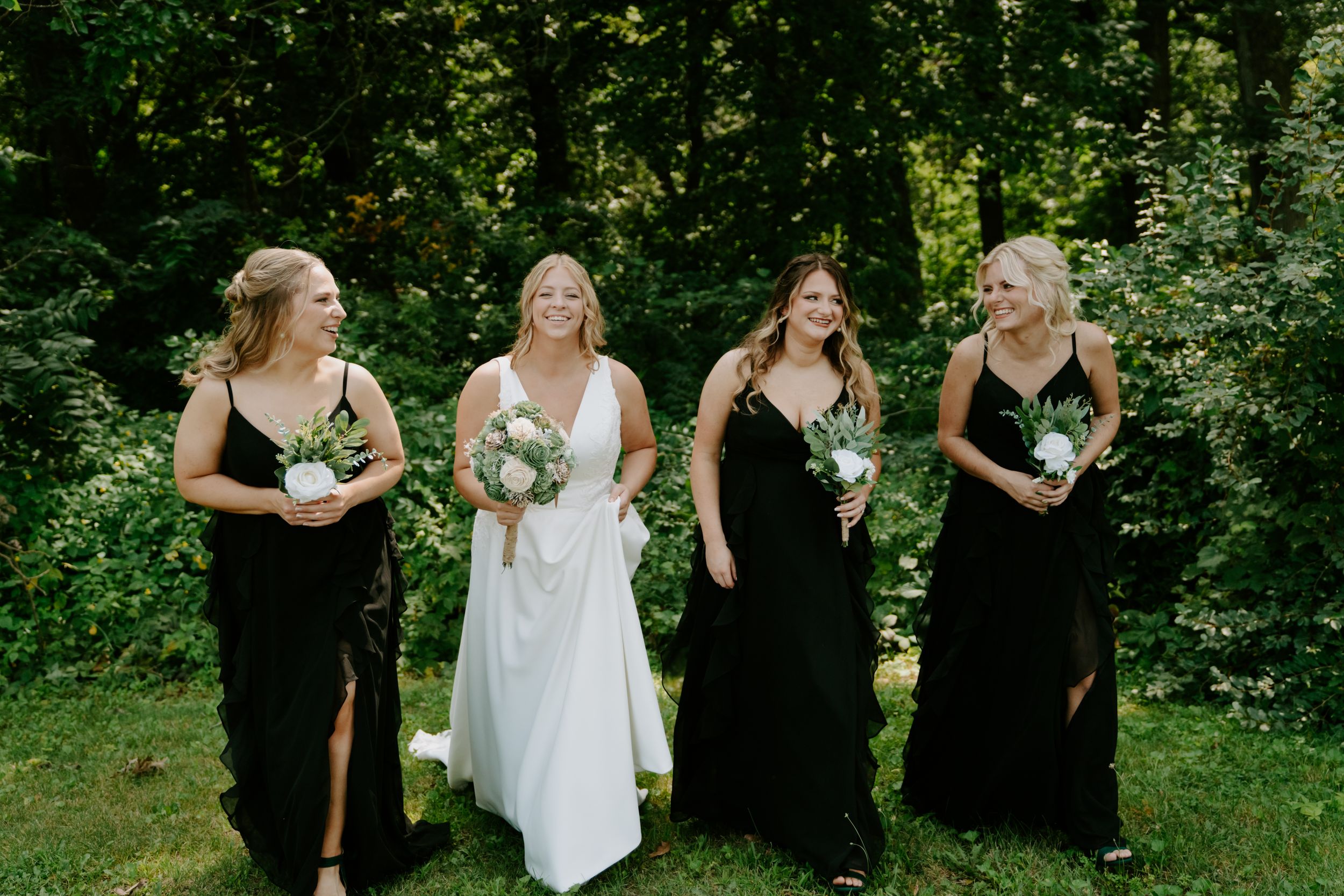 Wedding party in contrasting black and white dresses standing in a green forest setting.