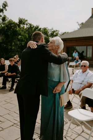 Wedding guest in teal dress views photo display during outdoor ceremony seating.