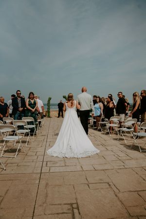 Outdoor wedding ceremony setup with white chairs and guests on a stone patio.