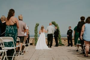 Wedding ceremony setup on an outdoor stone patio with white chairs and scenic mountain views in the background.