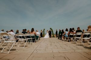 Guests seated in white chairs at an outdoor wedding ceremony with mountains visible in the distance.