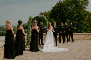 Wedding party arranged on a stone patio during an outdoor ceremony with greenery in the background.