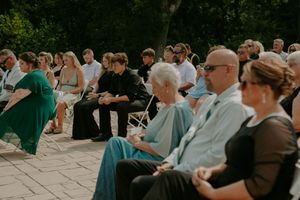 Wedding guests seated outdoors watching ceremony proceedings on a sunny day.