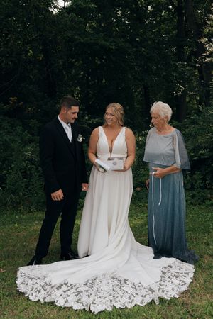 Wedding dress being adjusted on stone patio with detailed lace train spread out.