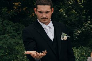 Groomsmen in black suits and white boutonnieres gathered outdoors during wedding ceremony.