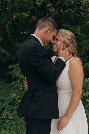 A romantic moment between newlyweds in formal attire surrounded by lush greenery.