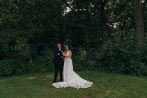 A tender moment between a couple in wedding attire against a natural backdrop.