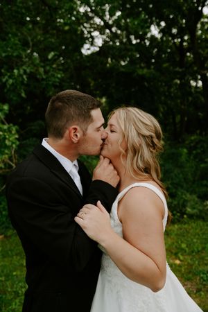A romantic kiss between newlyweds surrounded by lush summer foliage.