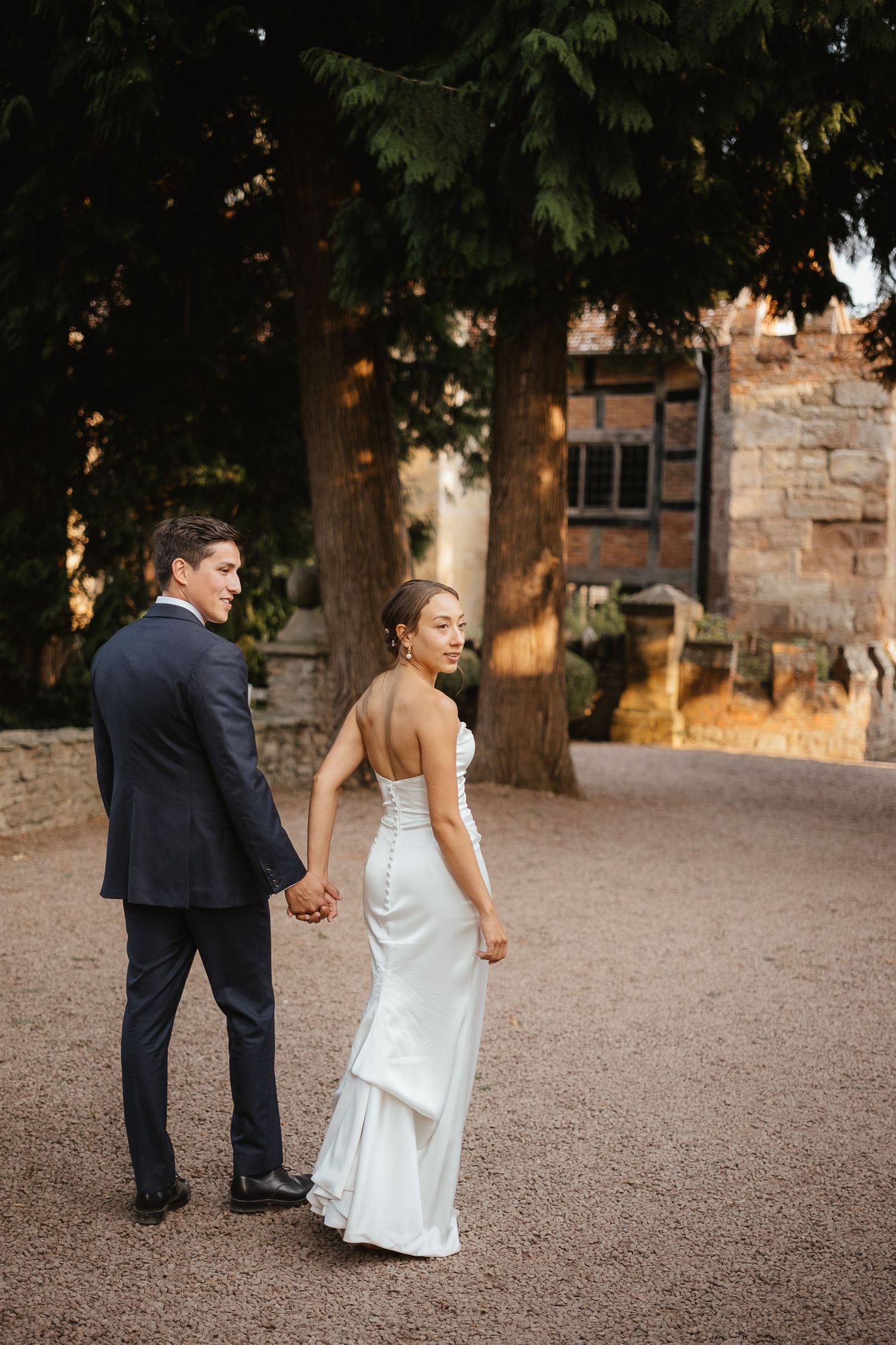 Couple shares intimate kiss during their first dance at wedding reception with brick wall backdrop and twinkling lights.
