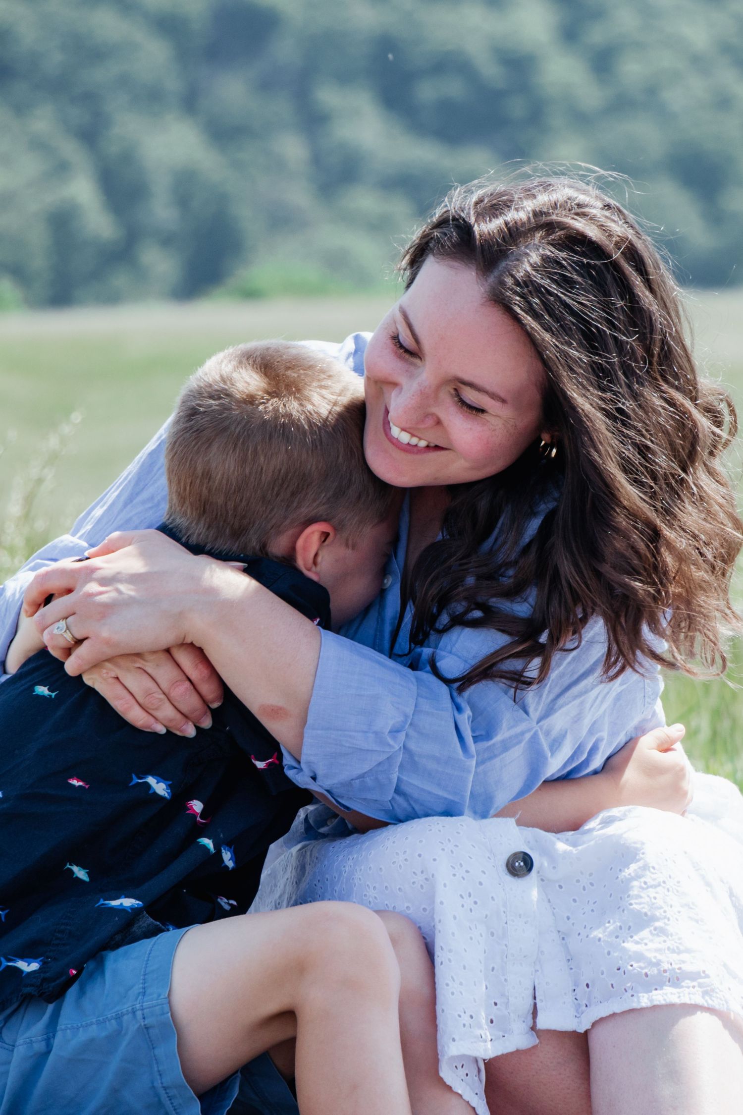 Smiling mother warmly embracing her young son during a candid outdoor moment in a sunlit field