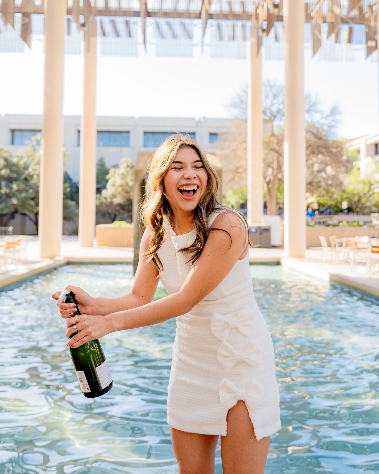 Woman in white dress celebrating with champagne bottle by pool.