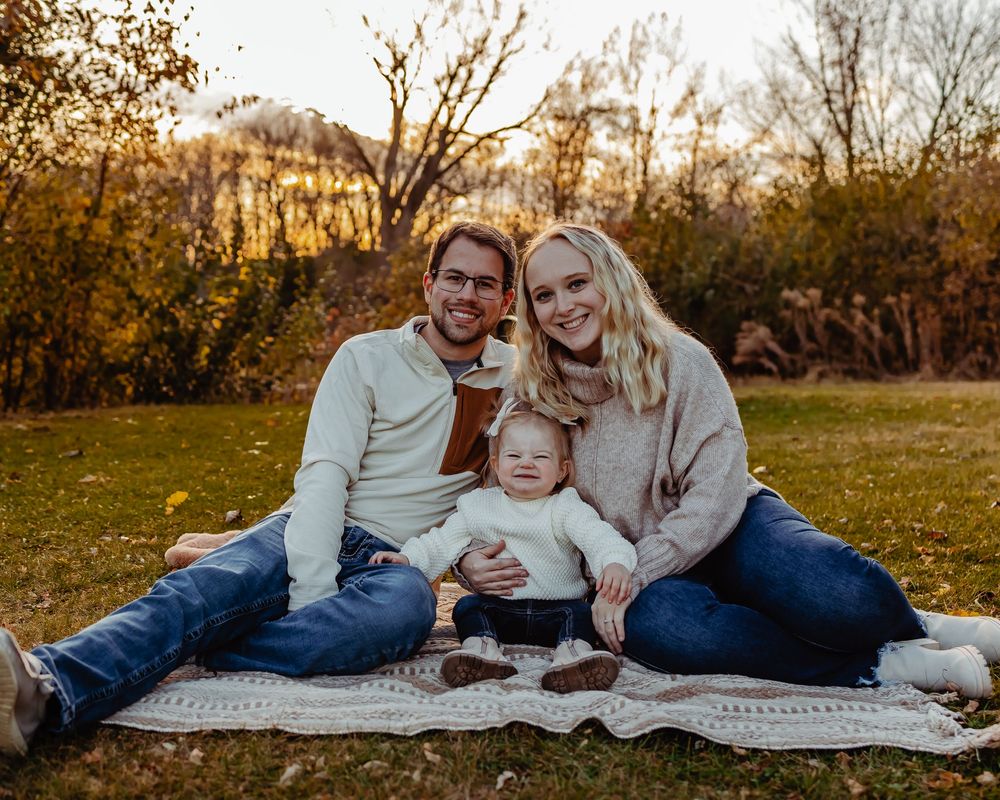 A family sits together on a blanket during a golden sunset in autumn while capturing a portrait moment.