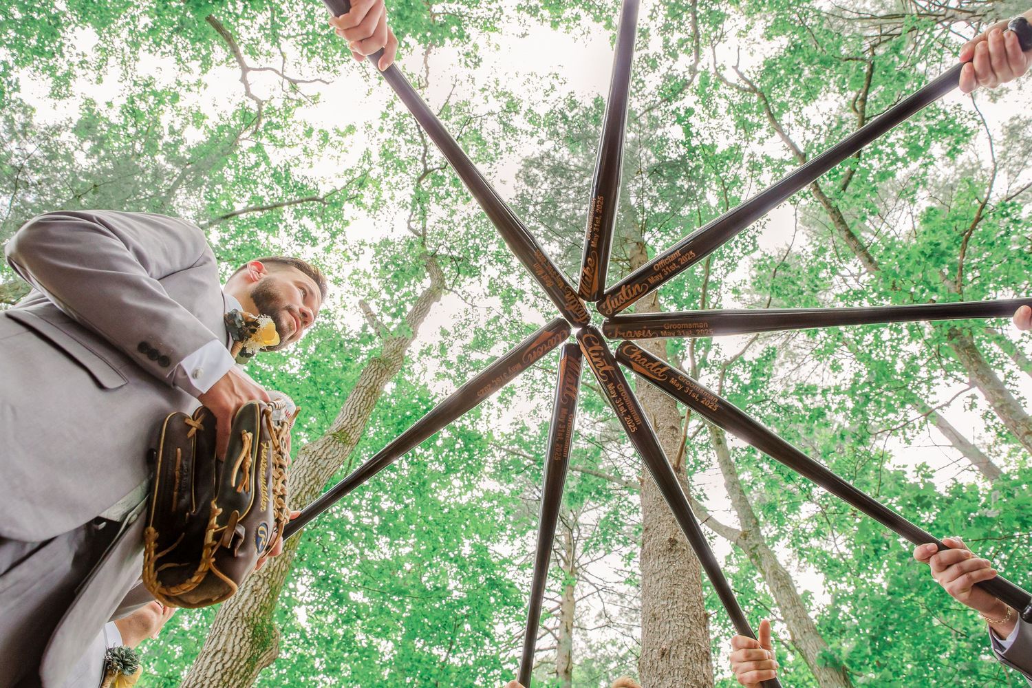 Looking up at large wooden beams in a radial formation against green tree canopy in a forest setting.
