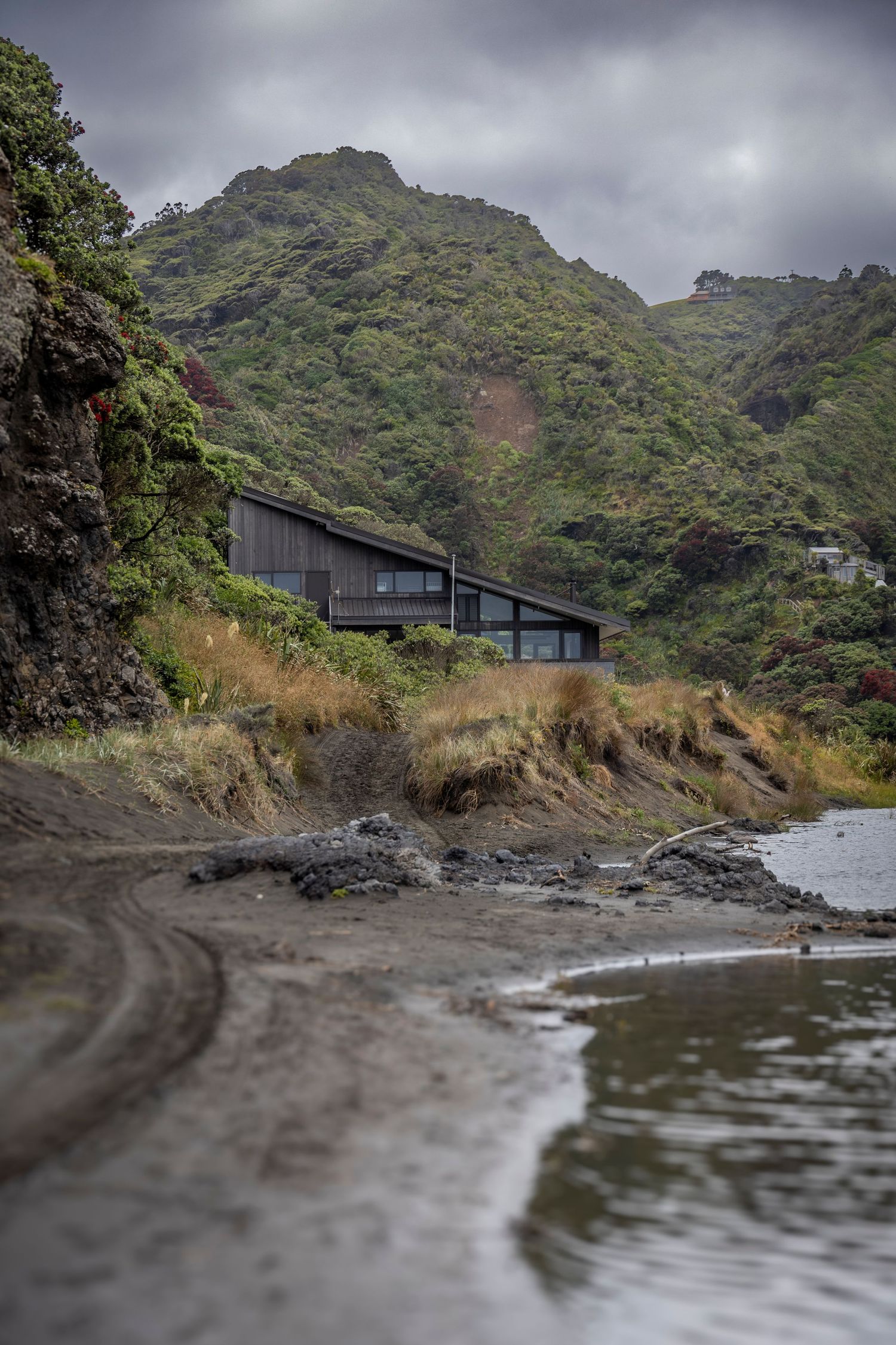 Contemporary beach house nestled in lush green cliffs overlooking a rocky shoreline and moody grey skies.