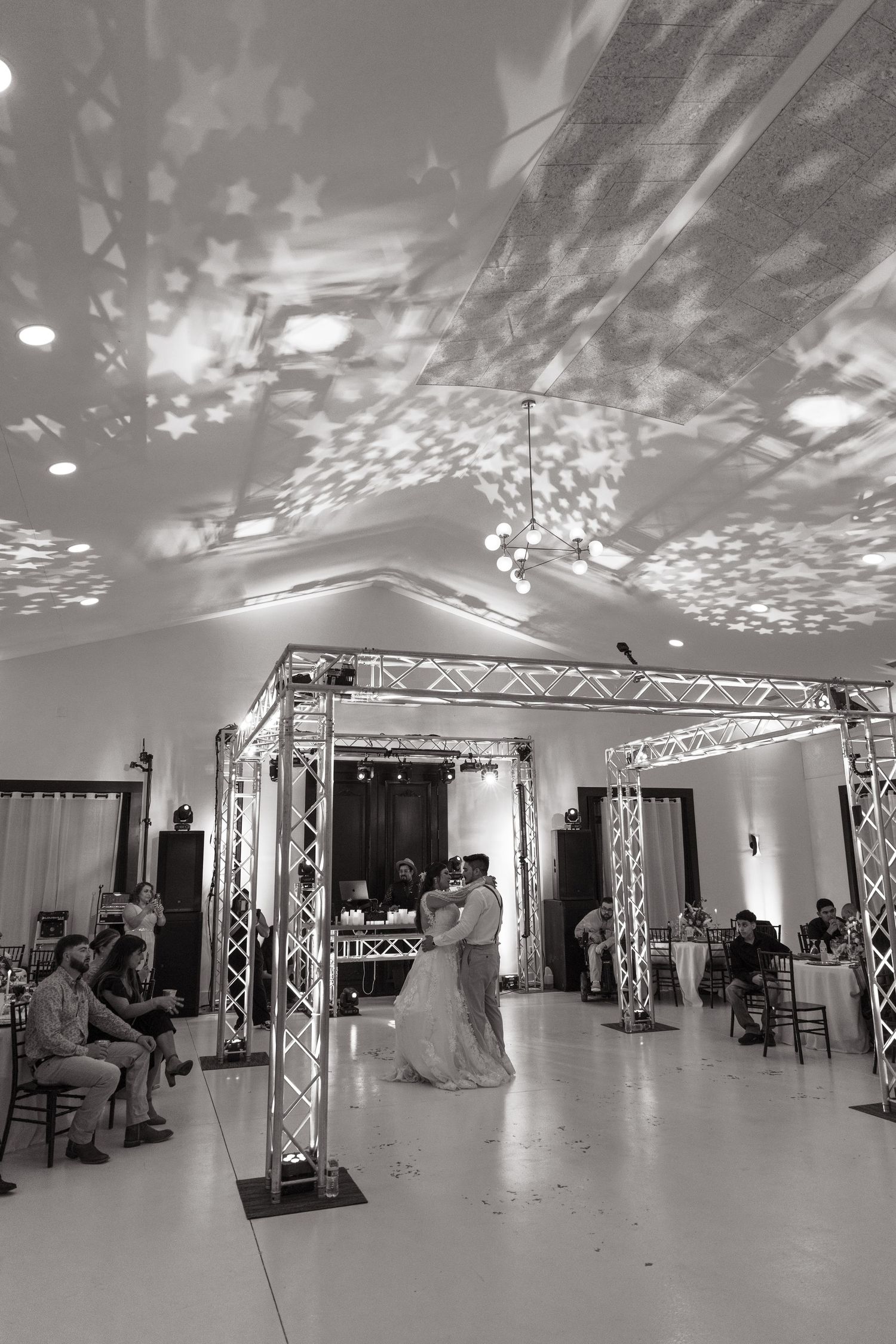 A wedding reception venue with couples dancing under a truss lighting system creating beautiful star-like patterns on the ceiling.