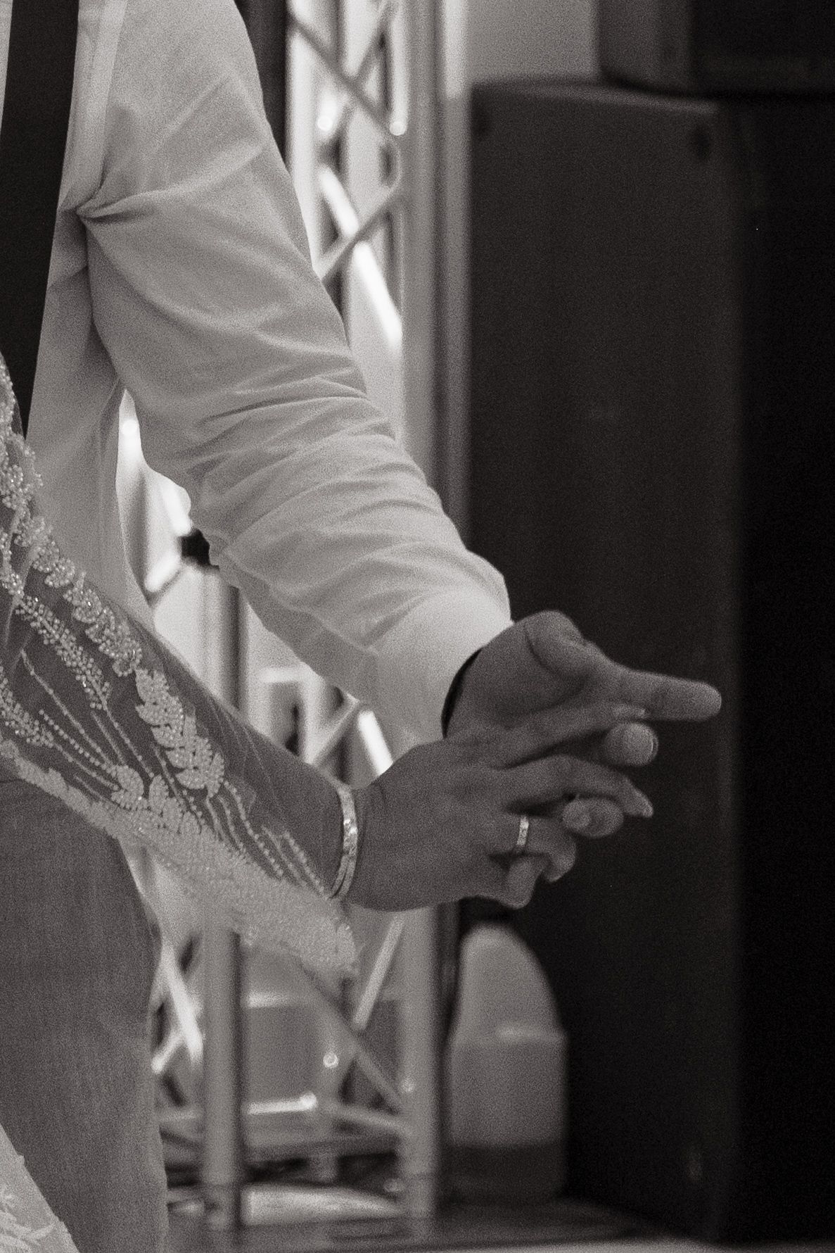 A black and white photograph captures two hands clasped together during a wedding ceremony.