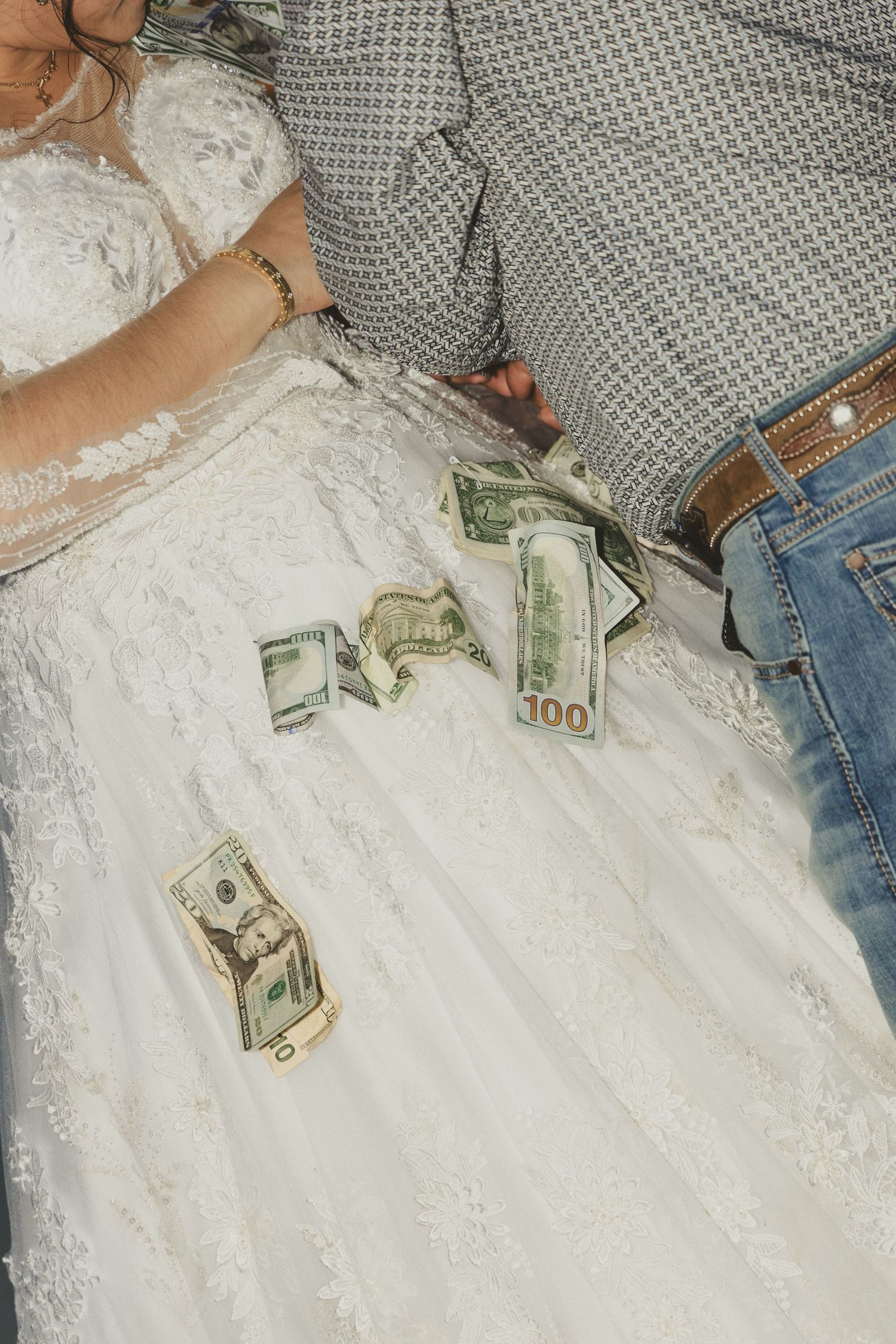 Cash bills scattered on a white wedding dress with denim and gray textiles visible in frame.