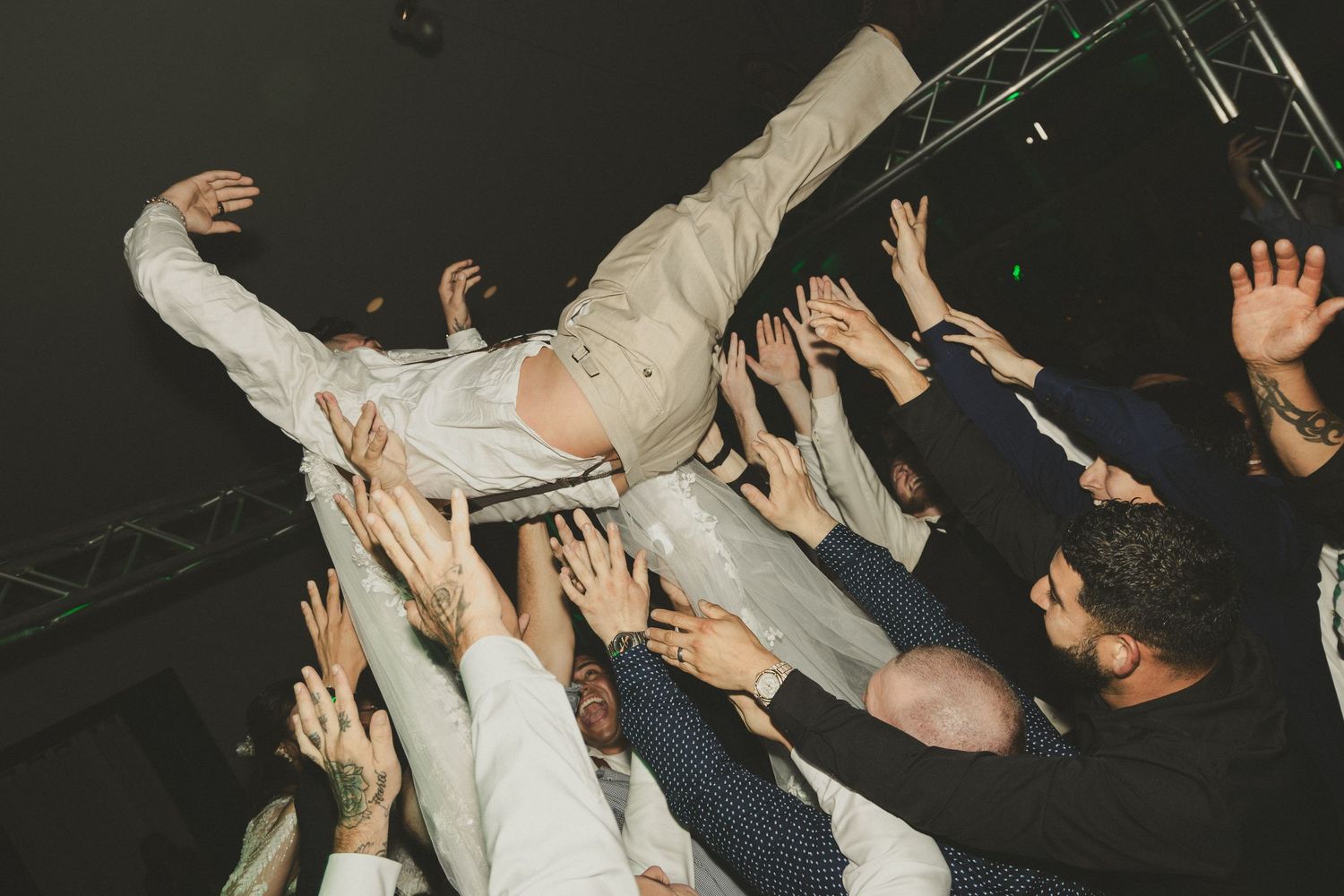 A person crowd surfing at a concert is supported by raised hands in the audience during an energetic performance.