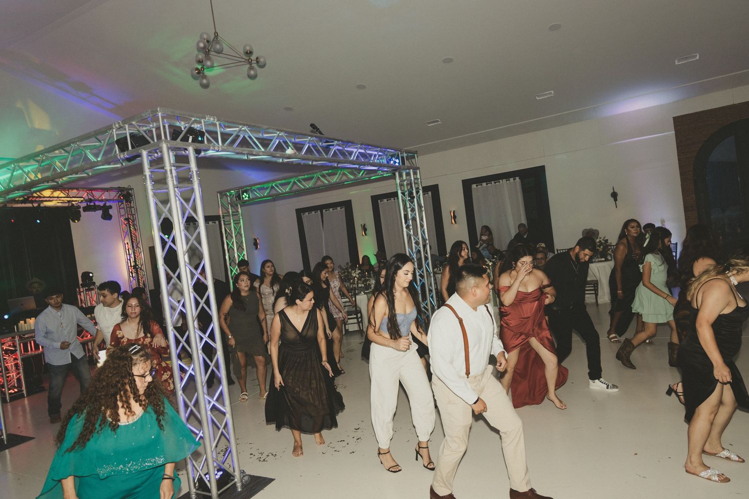 Partygoers dancing and mingling under stage lighting and metal truss at an indoor event space.