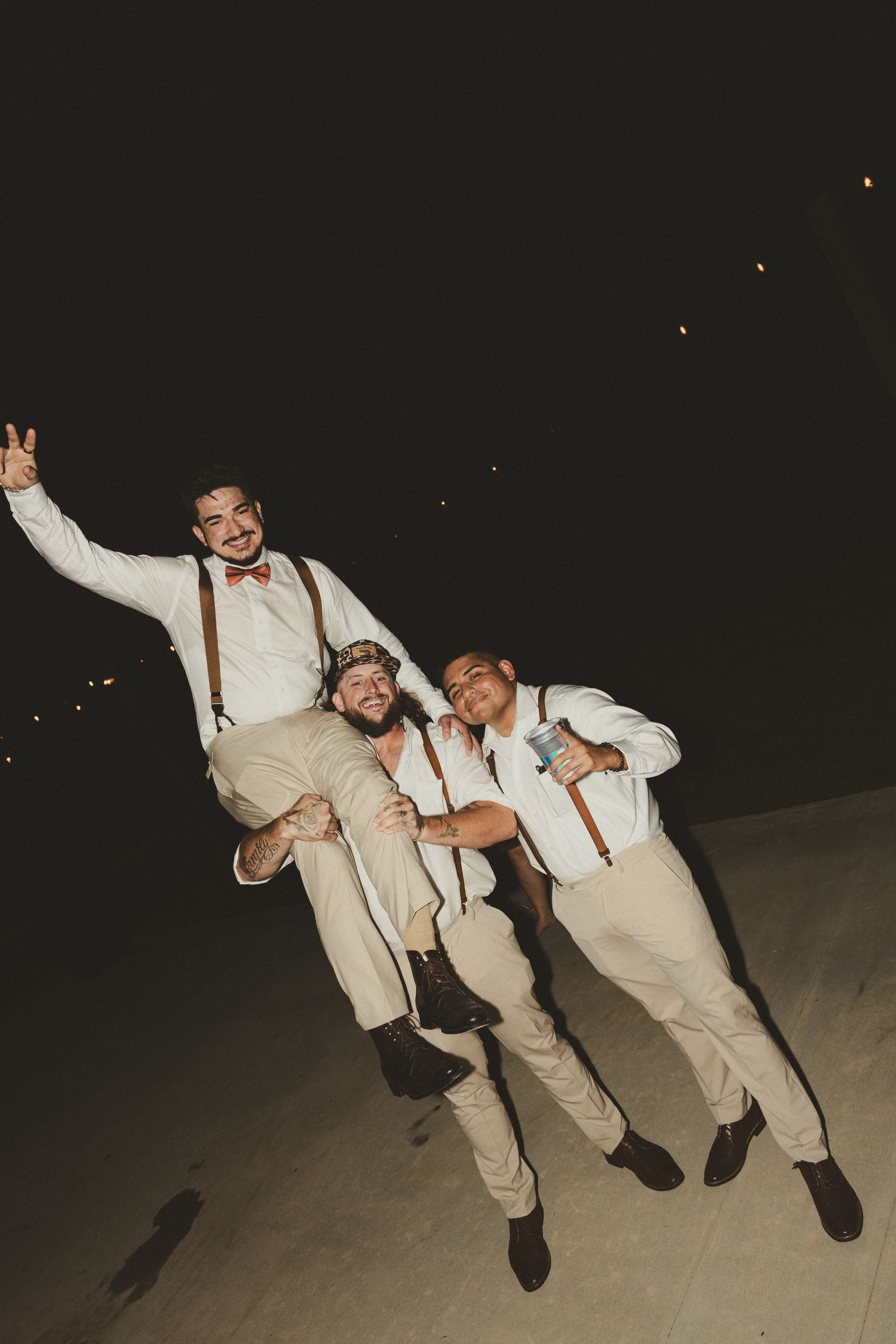 Four sequential photos show three people in beige suits jumping and posing together at a nighttime celebration.