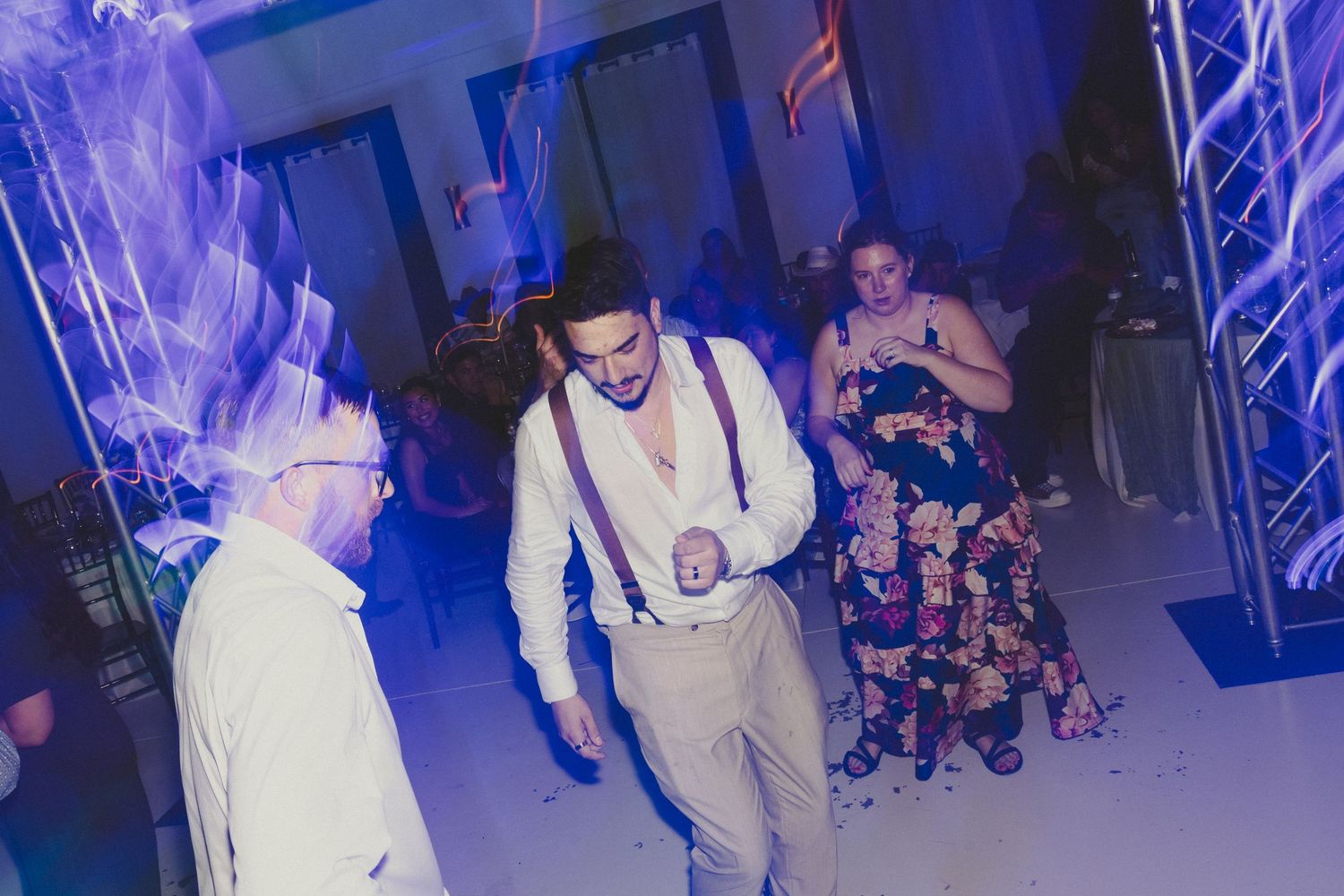 A group of people dancing joyfully at a wedding reception with purple lighting and dynamic party atmosphere.