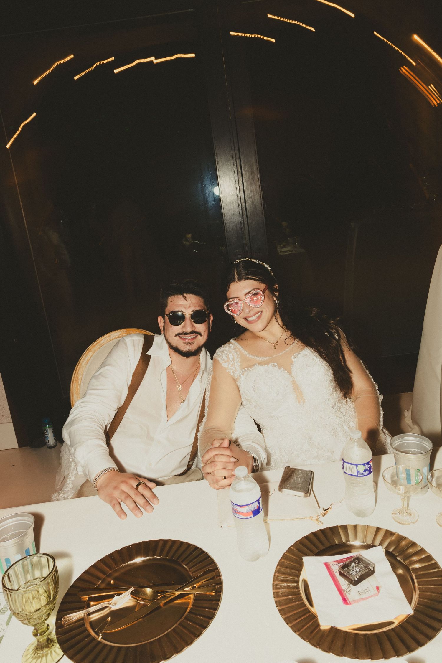 A couple sitting at an elegant dinner table with gold charger plates and candle light creating a warm ambiance.