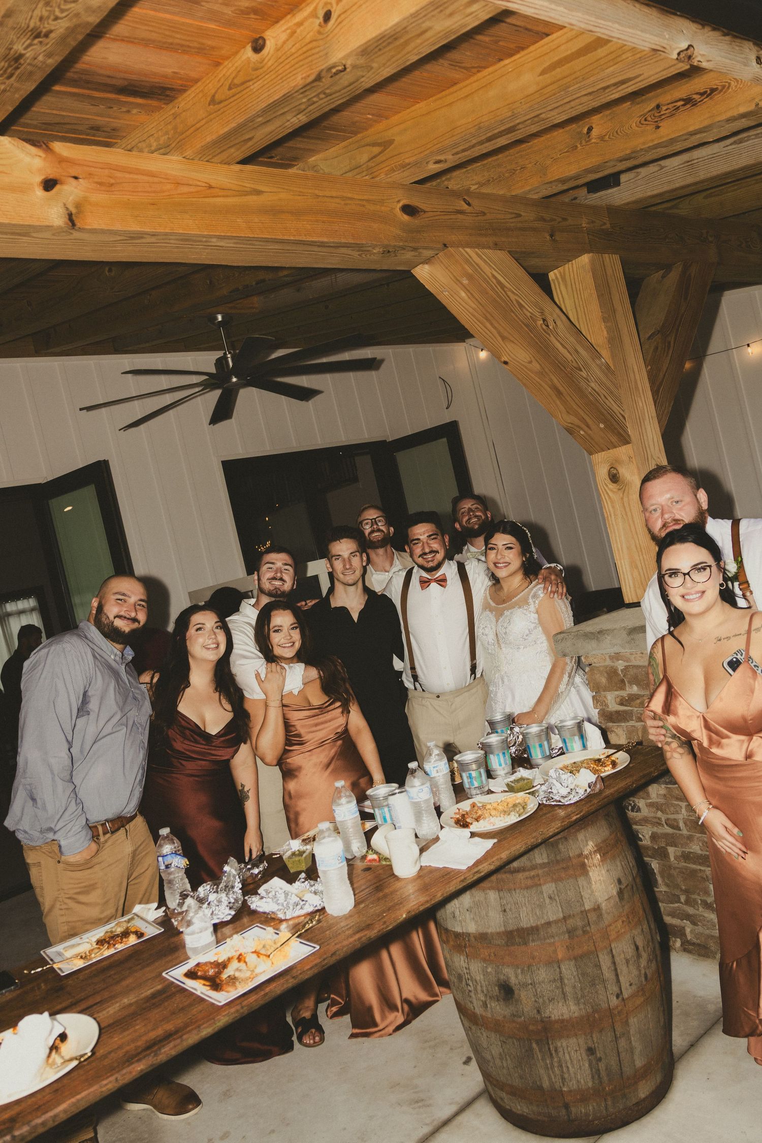 Rustic barn wedding reception features guests gathered around wooden barrel tables in a cozy vintage setting.