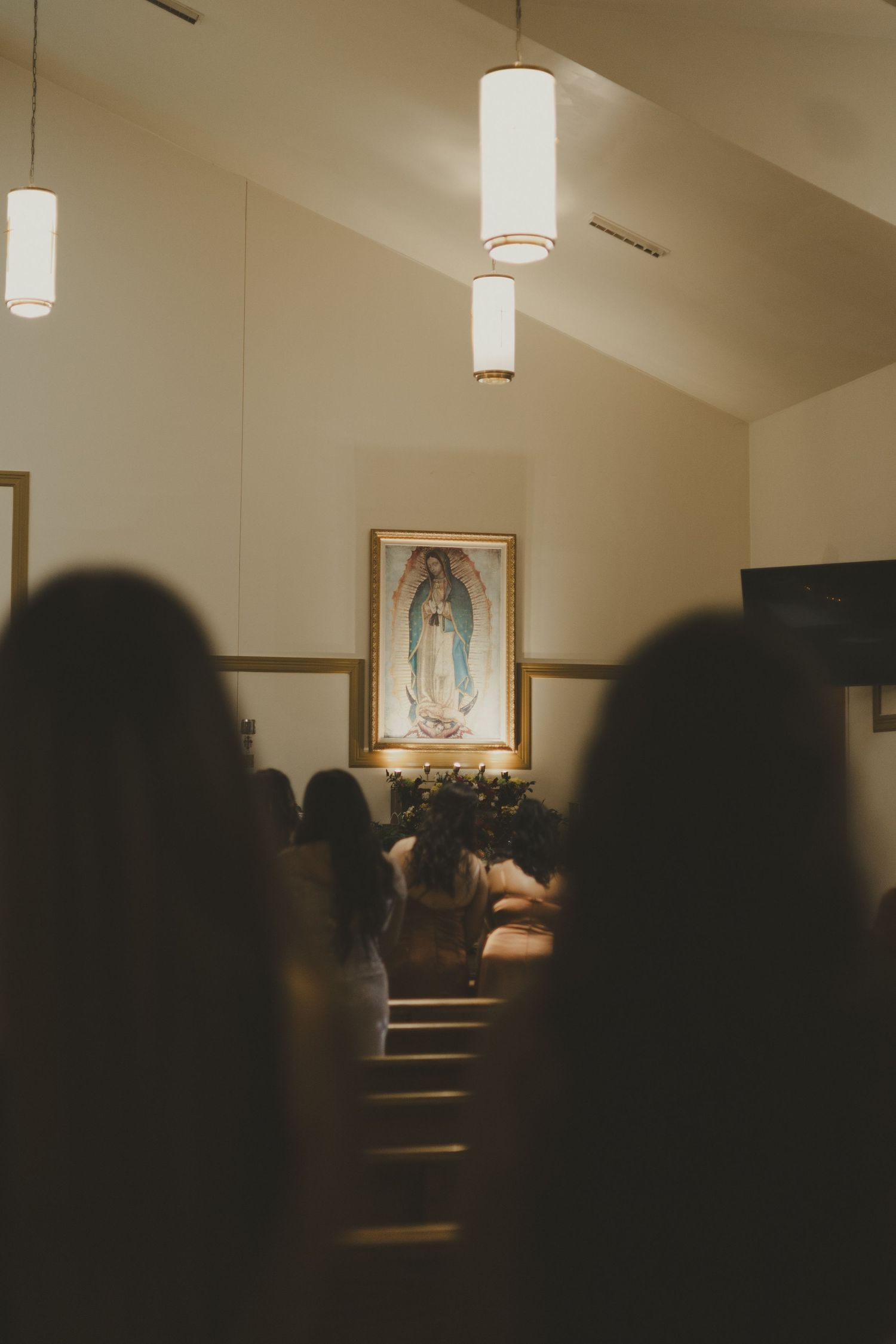 Church interior with hanging pendant lights and a painting of Our Lady of Guadalupe visible at the altar.