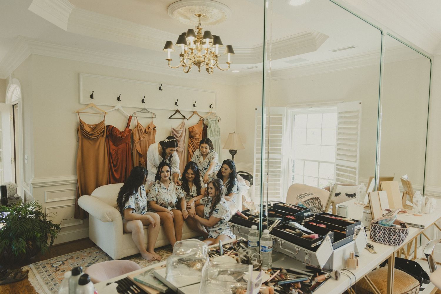Group gathered in cluttered dressing room with makeup tables and mirrors preparing for special occasion together.