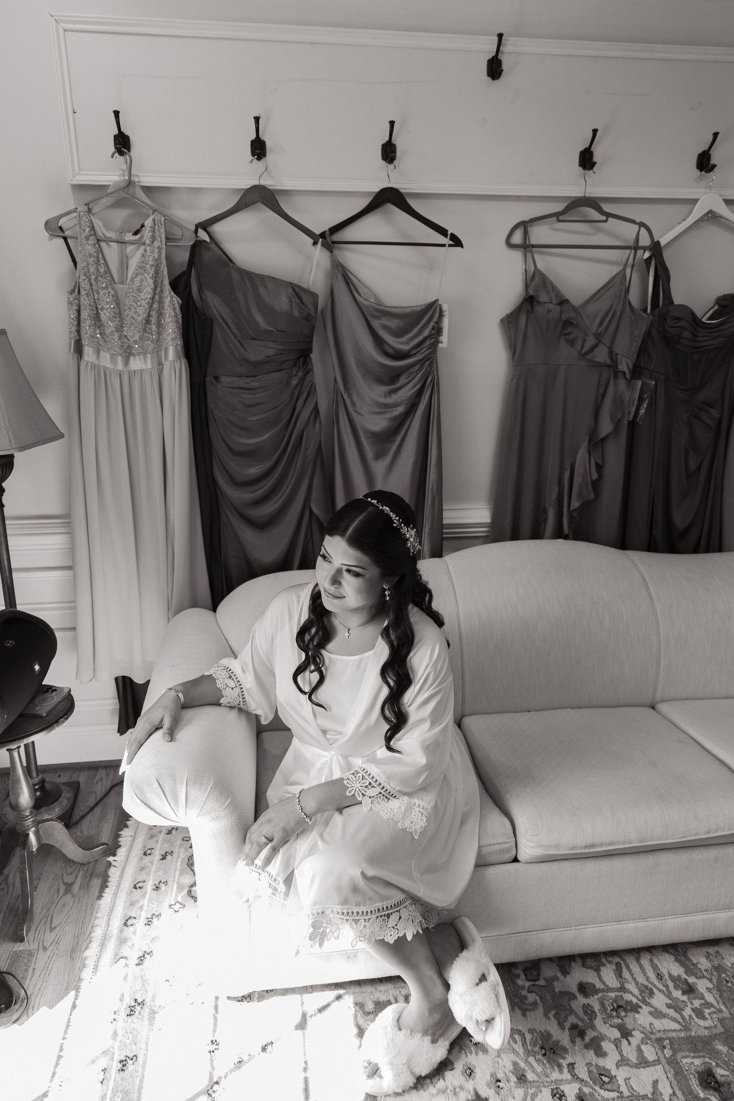 Black and white photograph with grey dresses hanging on wall hooks above a white couch with someone sitting in white attire.